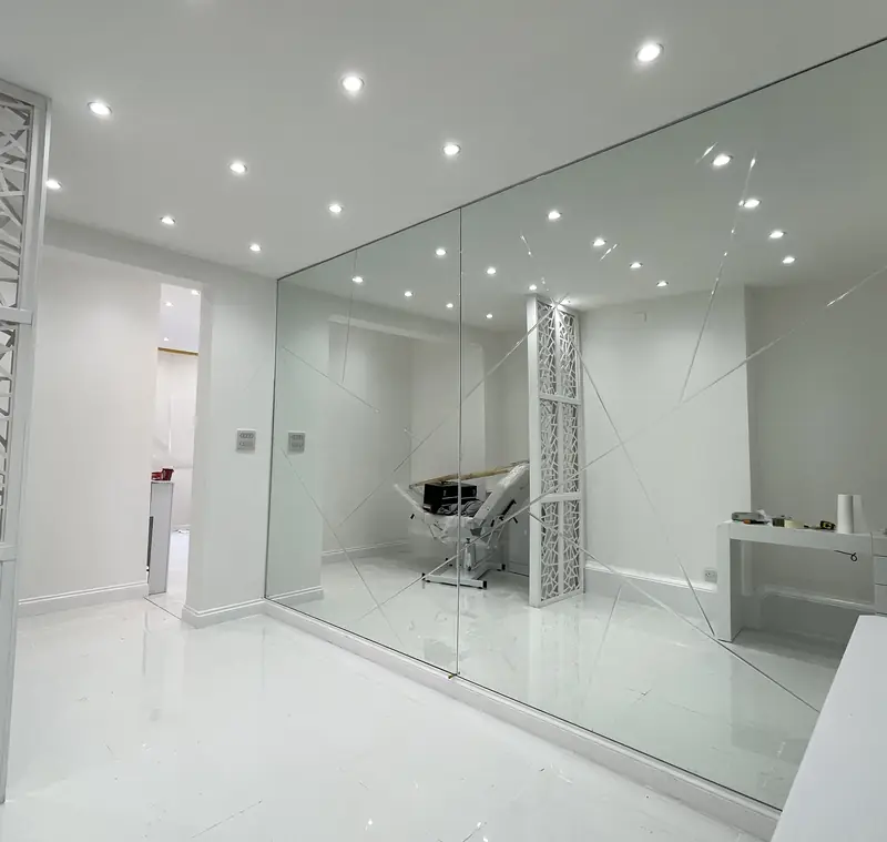 Floor-to-ceiling mirror wall with etched geometric lines in a white treatment room